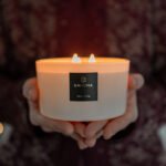 Beautiful noel noel white 3 wick candle offered as gift, held in hands