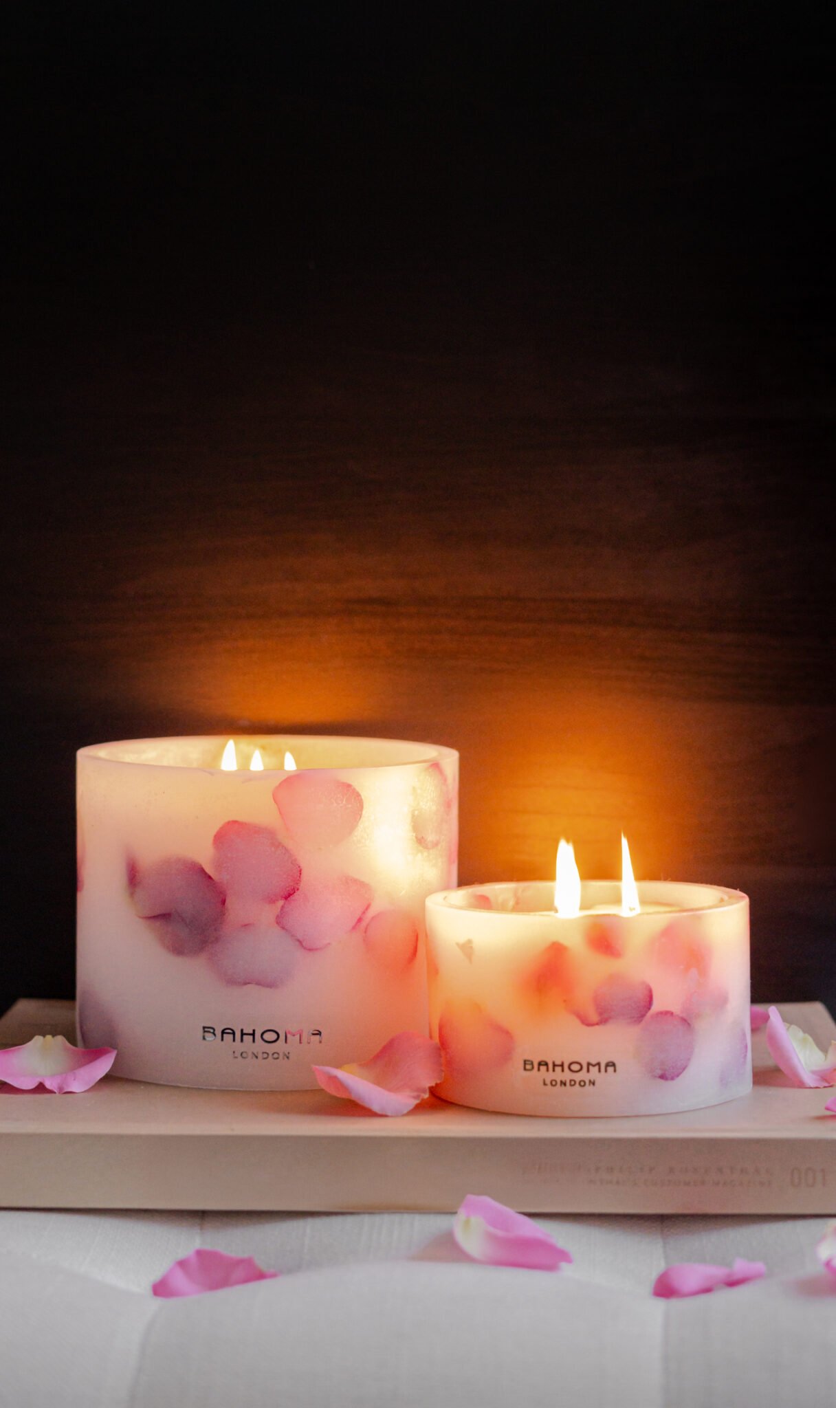 Lit up Velvet Rose - Small Pillar Candle made with real rose petals on a dark moody background with a glow, accompanied by a Grand pillar in same design