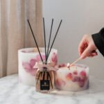 A hand lighting up Velvet Rose pillar candles with a diffuser in same fragrance
