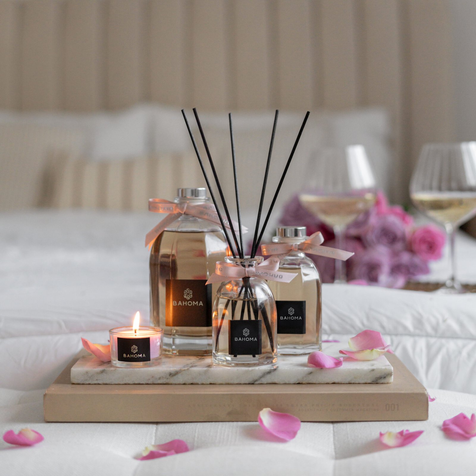 Velvet Rose - 500ml Fragranced Octagonal Diffuser with other size diffusers and travel candle arranged on a tray on a bed with rose petals scattered around.