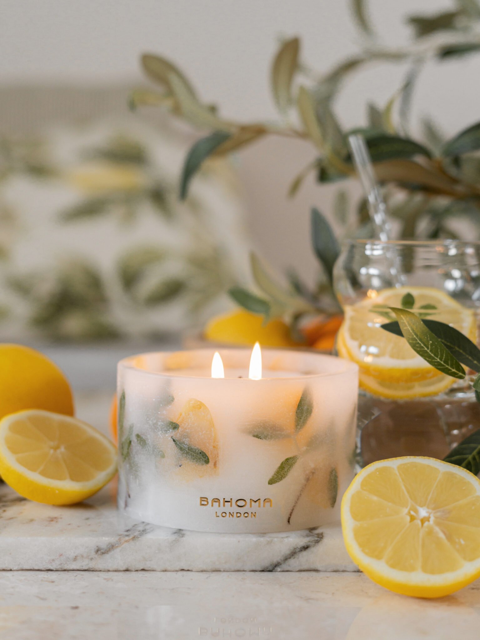 Amalfi Coast Scented Small Pillar Candle from the Bahoma Botanical Collection. Candle set on a wooden bench with a jug of lemonade in the background and fresh slices of lemon.